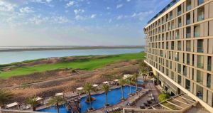 Backside view of Radisson Hotel Abu Dhabi featuring an open swimming pool, lush greenery, and a view of the Arabian Gulf. 