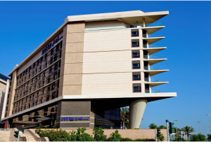 A daytime view of Park Inn by Radisson with a modern structure, surrounded by trees and set against a blue sky backdrop 